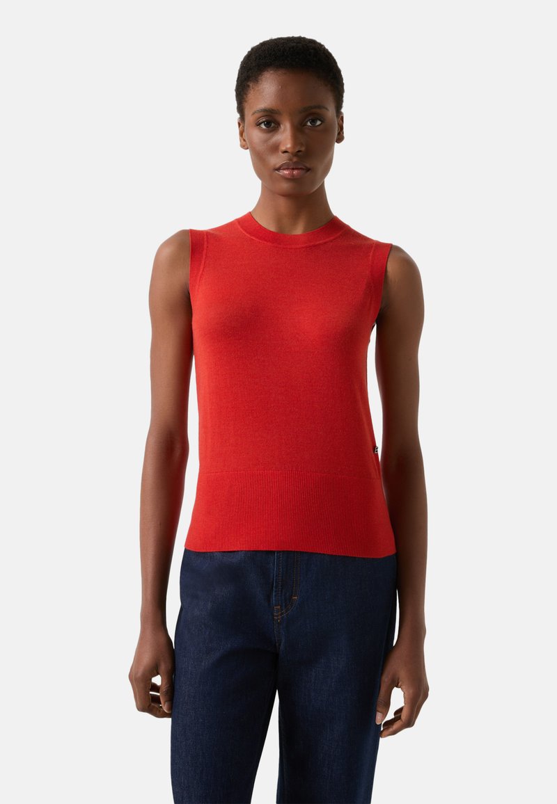 Czerwony top bez rękawów z dzianiny o gładkiej fakturze, z okrągłym dekoltem i dopasowanym krojem. Nosi się go z ciemnoniebieskimi dżinsami.