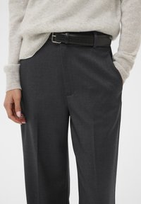 Gray tailored trousers with a smooth, textured fabric, paired with a light beige knit sweater and a black leather belt.