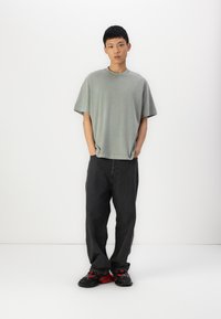 T-shirt cinza oversized de algodão com mangas curtas, combinada com calças de ganga escuras e sapatos pretos com detalhes em vermelho. Design simples e casual.