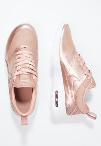 Par av metallisk rosaguld Nike-sneakers med vita sulor, synlig Air Max-dämpning, ovandel i mesh och syntetmaterial, sedd från ovan och sidan.