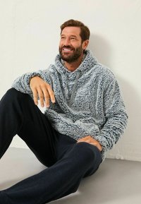 Grau fuzzy Kapuzensweatshirt aus strukturiertem Stoff, mit verstellbarem Kordelzug und vorderer Kängurutasche, kombiniert mit dunklen Jogginghosen.