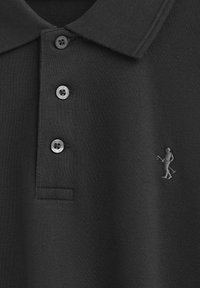 Svart polo skjorta med en strukturerad tyg, med tre knappar och en liten broderad figur i grått på vänster sida.