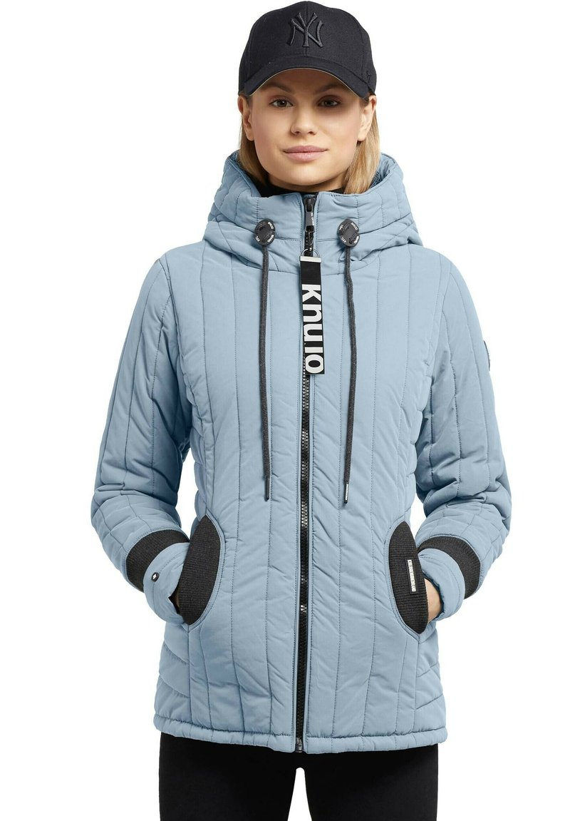 Himmelblau gesteppte Jacke mit Kapuze, schwarzen Akzenten an den Bündchen und Taschen, Frontreißverschluss und Kordelzug, mit einem Logetiketter am Reißverschluss.