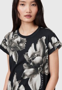 Camiseta negra con grandes estampados de flores en blanco y negro, cuello redondo y mangas cortas; logo "ALLSAINTS" en un lateral.
