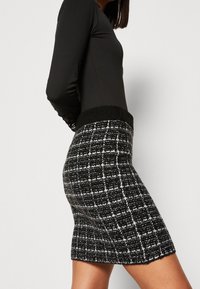 Černo-bílá kostkovaná pletená sukně s žebrovaným černým pasem, přiléhavý silueta a jemná textura, dosahující délky do poloviny stehna.