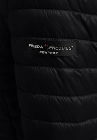 Zwarte pufferjack met een gewatteerde textuur, voorzien van een merklabel met de tekst "FRIEDA FREDDIES NEW YORK" in het wit en rood.
