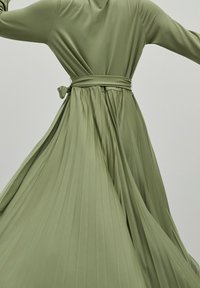 Lång olivgrön klänning med plisserad design, midjerem med snörning och flytande tygstruktur, med långa ärmar och en slät silhuett.