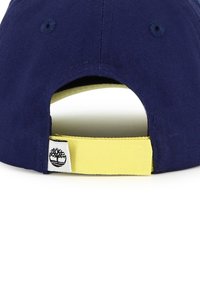 Cappellino blu navy con cinturino regolabile giallo. Presenta un tessuto strutturato, occhielli circolari e un piccolo cartellino con logo sul cinturino.