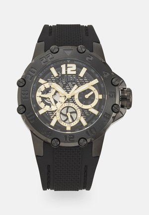 Montre chronographe noire avec un cadran noir texturé, des accents dorés et un bracelet en caoutchouc. Comprend des index d'heure audacieux et une lunette à motif.