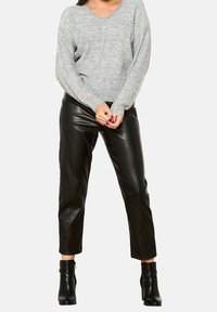 Grauer, übergroßer V-Ausschnitt-Pullover kombiniert mit schwarzen, eng anliegenden Lederhosen und Stiefeletten, die eine glatte Textur und ein elegantes Design zeigen.