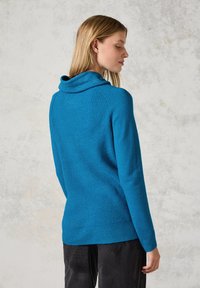 Pull en tricot turquoise avec un col roulé, texture côtelée et manches longues, présenté de dos sur un fond neutre clair.
