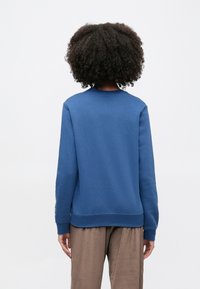 Μπλε φούτερ με στρογγυλή λαιμόκοψη, μανσέτες και τελείωμα με ριμπ ύφανση. Μαλακή υφή, άνετη γραμμή, συνδυάζεται με καφέ άνετο παντελόνι.