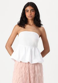 Biela top bez ramienok s nariaseným peplum okrajom, skombinovaná s ružovou sukňou s volánmi, predvádzajúca jemnú textúru látky a vrstvený dizajn.