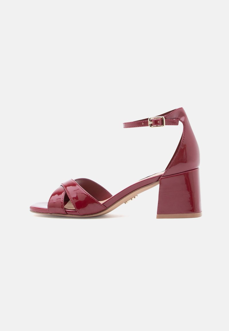Κόκκινα δερμάτινα σανδάλια με τακούνι και λουράκι στον αστράγαλο, με ανοιχτά δάχτυλα, διασταυρωμένα λουράκια και σχέδιο με χοντρό τακούνι. Διακοσμητικά στοιχεία σε χρυσό.