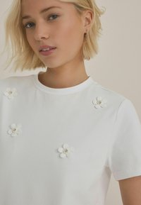 Hvid kortærmet t-shirt med blomsterapplikationer med perlecentre, rund halsudskæring og glat bomuldsstruktur.