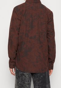 Brun strukturerad skjorta med svarta abstrakta mönster, långa ärmar, knäppning vid ärmslut och klassisk krage. Bärs med grå slitna jeans.