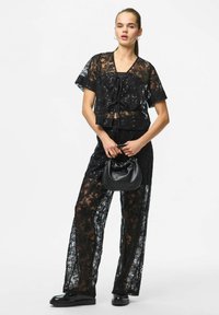 Czarny dwuczęściowy zestaw z koronką, składający się z krótkiego topu z krótkim rękawem i cekinami oraz spodni o szerokich nogawkach. Akcesoria obejmują małą czarną torebkę.