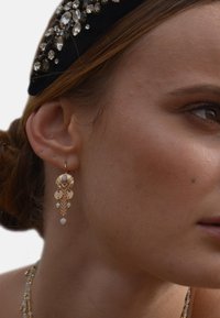 Boucles d'oreilles en or avec des motifs complexes mettant en valeur des perles et des accents suspendus. Cette pièce maîtresse allie élégance et finition texturée.