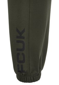 Olijfgroen katoenen sweatpants met een taps toelopend ontwerp, voorzien van een zwart bedrukt logo langs de linkerkant en elastische boorden bij de enkels.
