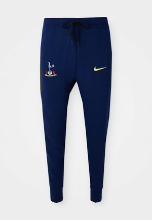 Námornícke tepláky s vyšitým logom na hornej ľavej nohe a malým žltým Nike swooshom na dolnej pravej nohe.