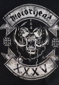 Černé tričko s velkým bílým grafickým vyobrazením vrčící lebky zvířete s rohy, obklopené dekorativními prvky a textem "Motörhead XXXV."