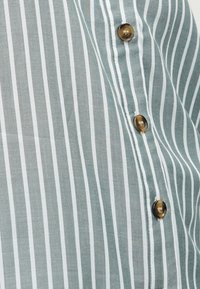 Κατακόρυφο ύφασμα με πράσινες και λευκές ρίγες και τρία διαφανή καφέ κουμπιά ραμμένα κατά μήκος μιας ραφής.