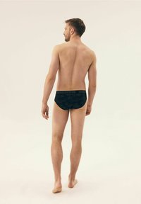 Czarna bielizna z wzorzystym wzorem i markowym pasem, noszona przez modela męskiego od tyłu, z naciskiem na dopasowanie i sylwetkę.