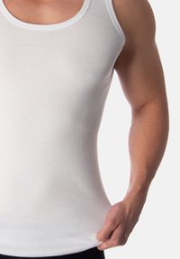 White tank top made of cotton, featuring a round neck, fitted design, smooth texture, and minimal seams, held at the hem by a hand.