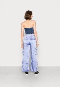 Top azul sem alças com acabamento texturizado, combinado com calças cargo largas de cetim roxo claro com múltiplos bolsos.