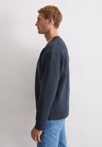 Granatowy sweter z okrągłym dekoltem, z prążkowanymi mankietami i dolnym brzgiem, wykonany z miękkiego materiału, w połączeniu z jasnoniebieskimi dżinsami.