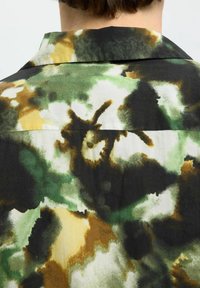 Kurzarmhemd mit einem Aquarell-Tarnmuster in Grün-, Braun- und Schwarztönen; leichtes Material mit einer glatten Textur.