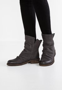 Bottes de cheville grises avec une finition texturée, un design décontracté et une large ouverture en haut. Le talon en bois robuste ajoute un contraste au matériau.