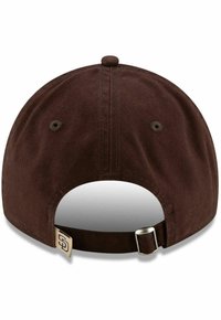 Casquette de baseball en coton marron avec une visière courbée, sangle ajustable à l'arrière et étiquette avec logo brodé. Tissu texturé, forme arrondie.