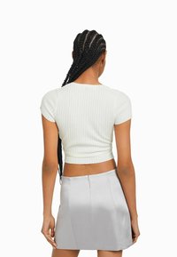 Ljusgrön, cropped ribbad topp med korta ärmar, i kombination med en silverfärgad satin kjol. Bakifrån visas en figurnära design och texturerad tyg.