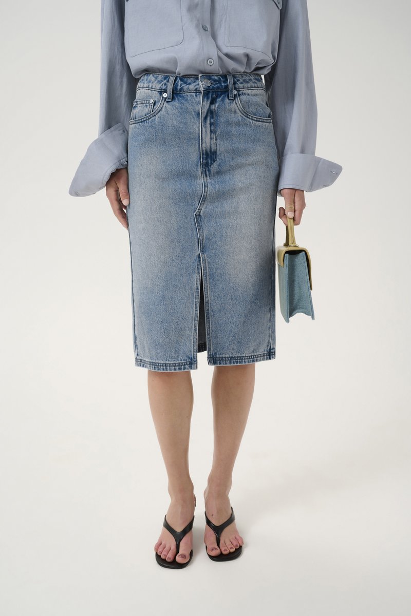 Γαλάζια τζιν μολυβένια φούστα με μπροστινή σχισμή, ψηλή μέση και ακατέργαστο στρίφωμα. Συνδυάζεται με μαύρα παντόφλες και μια μικρή μπλε τσάντα.