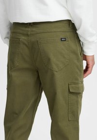 Olive green cargo pants featuring a textured fabric, two back pockets, and a side pocket with a flap. The design includes visible stitching details.