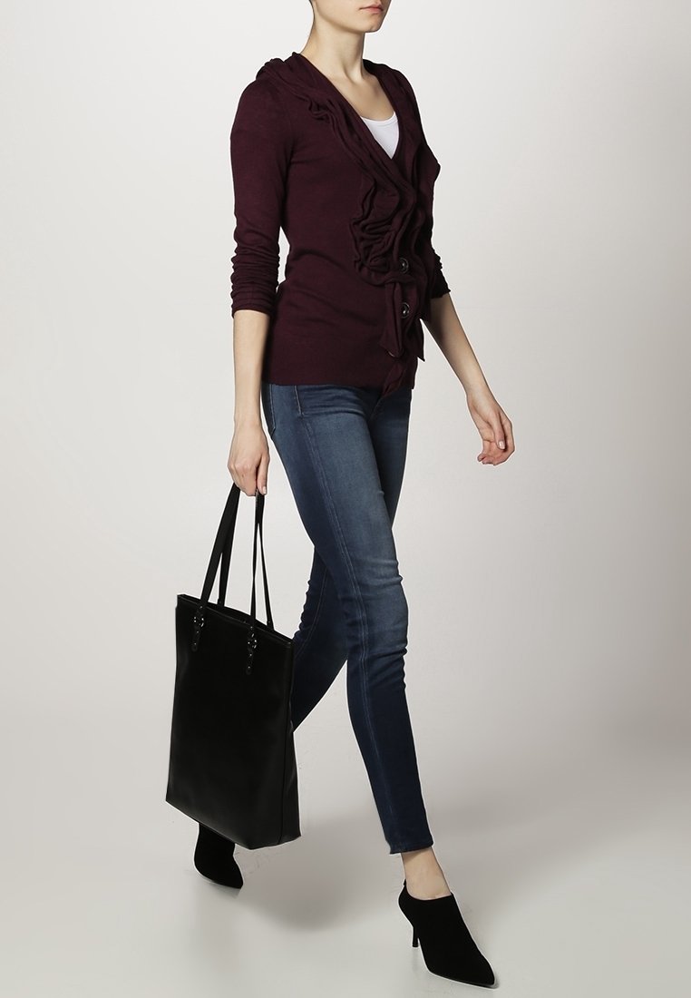 Bordowy sweter rozpinany z falbanami i guzikami, zestawiony z niebieskimi dżinsami i czarną torebką. Modelka nosi czarne szpilki w szpic.