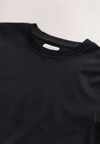 Juoda medvilninė marškinėliai su klasikine apvalia kaklo linija, soti tekstūra ir subtiliu prekės ženklo ženklu ant vidinės apykaklės.