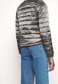 Polstret grå jakke med blank finish og vandret quiltet mønster. Kombineret med blå denim, der viser kontrasterende teksturer.