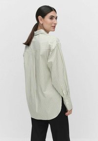 Light green striped shirt with a full-length back, button cuffs, and a rounded hemline. Made from smooth fabric with a slightly oversized fit.