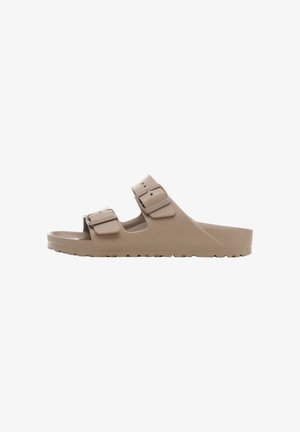 Beige rubberen sandalen met twee verstelbare bandjes, een gestructureerde voetbed en een lichtgewicht ontwerp. De zool heeft een gemarmerde grip voor tractie.