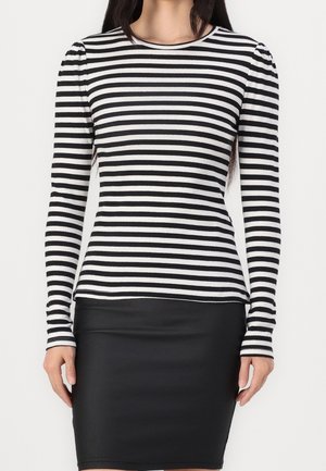 Femme portant un haut à manches longues rayé horizontalement noir et blanc, associé à une jupe noire ajustée longueur genou.