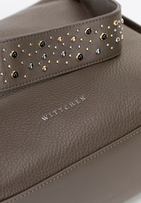 Brązowa skórzana torebka z teksturowaną powierzchnią i szerokim paskiem ozdobionym metalowymi ćwiekami w kolorze złotym, srebrnym i czarnym. Widoczne srebrne logo marki.