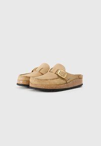 Mocassins en cuir beige à bout rond, avec un accent de boucle dorée et une semelle intermédiaire brun en liège sur une semelle extérieure en caoutchouc noir.