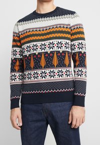 Stickad tröja med marinblå bakgrund och multicolor geometriska och trämönster i orange, vitt och grönt. Ribbade muddar och nederkant.