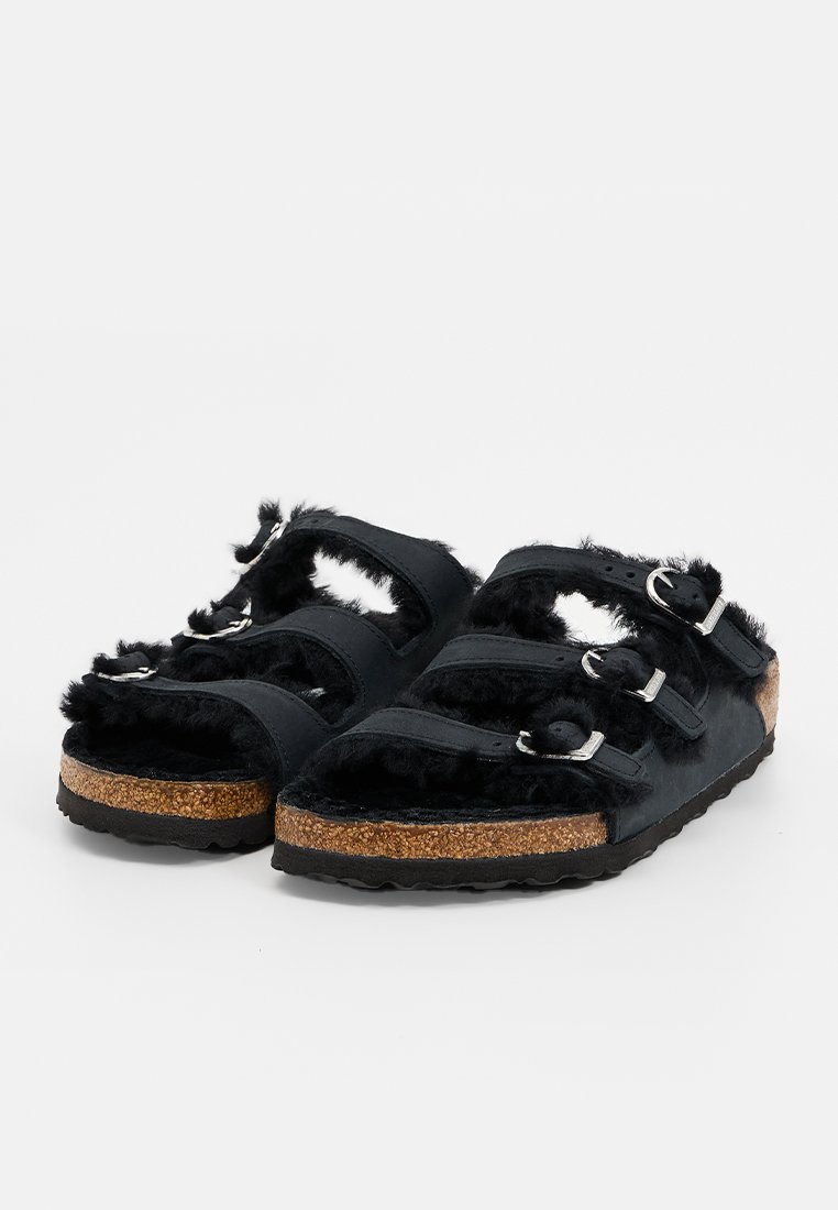 Sandali neri in pelliccia sintetica con tre fasce regolabili, fibbie in argento e una suola interna in sughero testurizzato. Suola esterna in gomma antiscivolo.