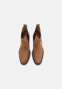 Botas de tobillo de ante marrón con paneles laterales elásticos, punteras redondas y suelas de goma negra. Presentan una lengüeta en la parte posterior para facilitar el uso.