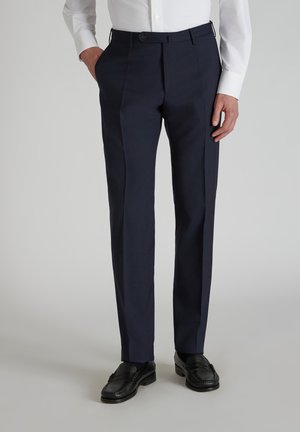 Pantalones de vestir azul marino con un corte a medida, con frente plano, bolsillos laterales y una textura suave, combinados con mocasines negros.