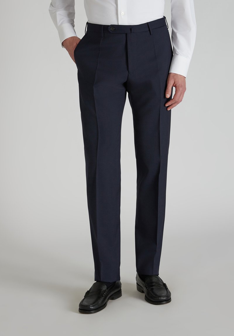 Marineblaue Stoffhosen mit taillierter Passform, flacher Front, seitlichen Taschen und glatter Textur, kombiniert mit schwarzen Slippern.