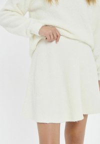 Witte, gestructureerde, knielange rok met een uitlopend ontwerp. De stof lijkt zacht en comfortabel, met een licht fuzzy afwerking.